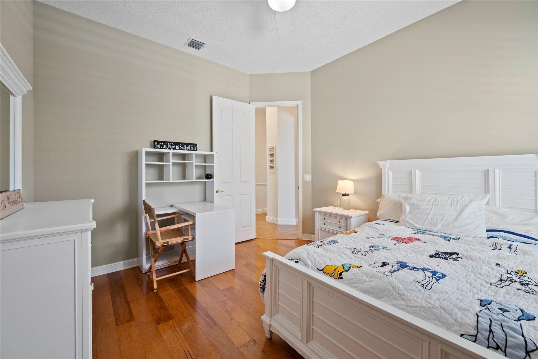 Bedroom with white furniture, hardwood floors, a patterned quilt, and a small desk.