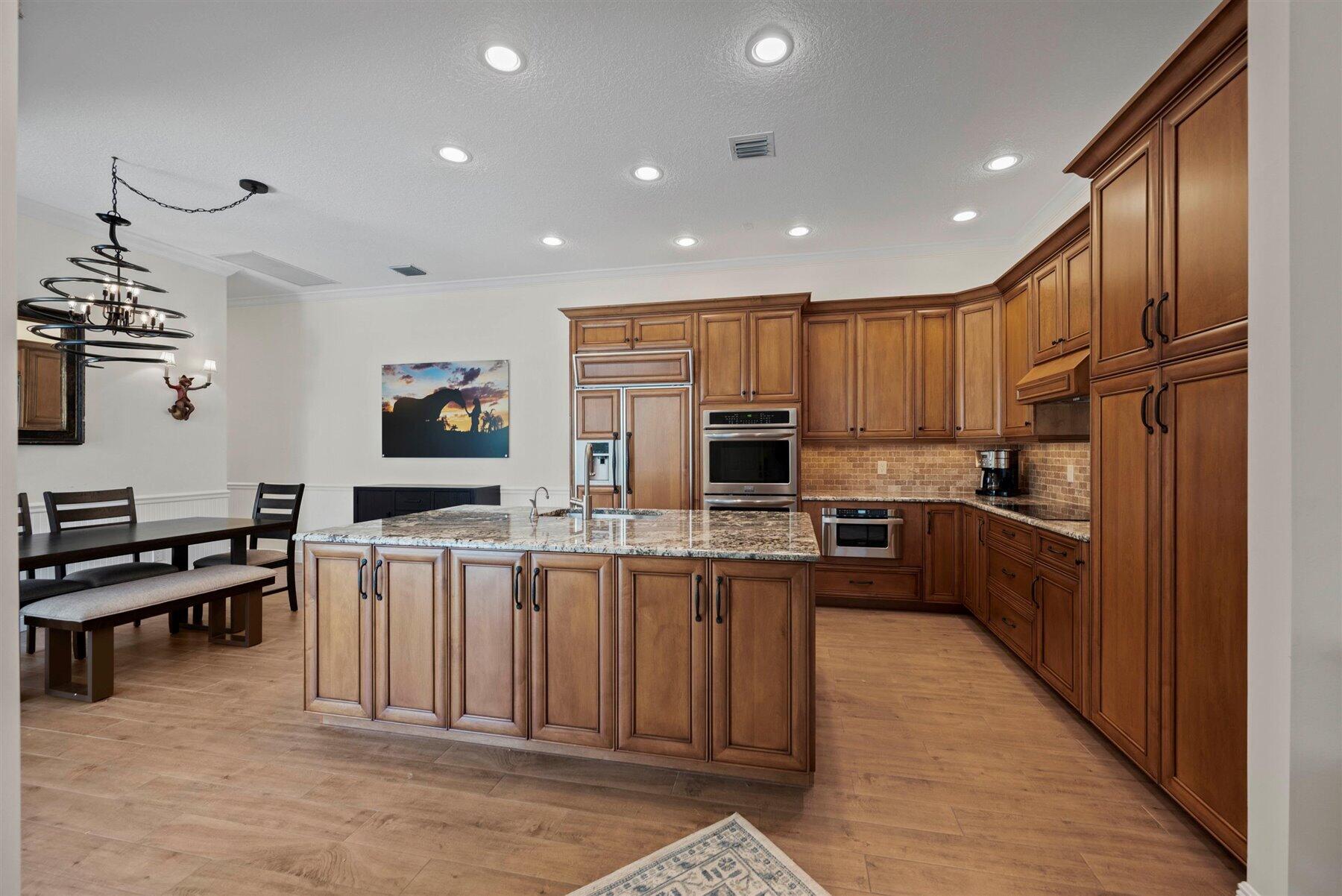 Kitchen with warm wood cabinetry, a large granite island, and stainless steel appliances.