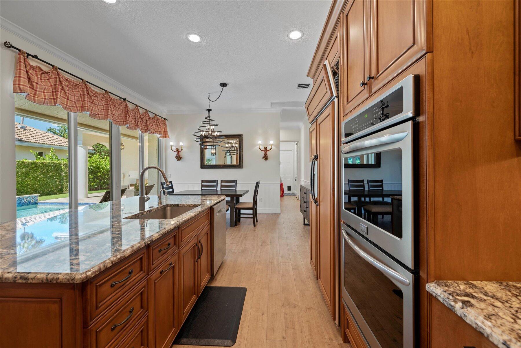 Kitchen with wood cabinets, granite island, built-in ovens, and sliding doors overlooking a pool.