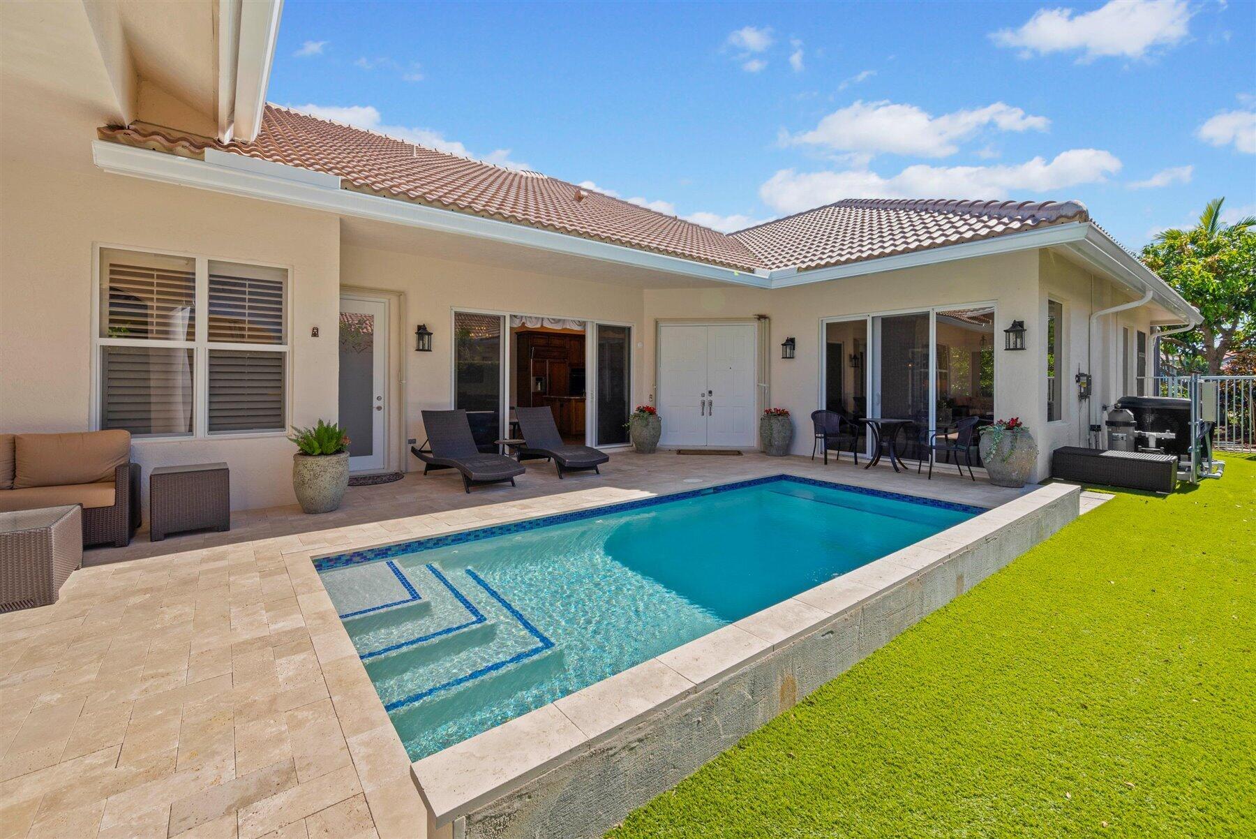 Home’s rear patio and rectangular pool, with lounge chairs, outdoor dining, and a terracotta tile roof.