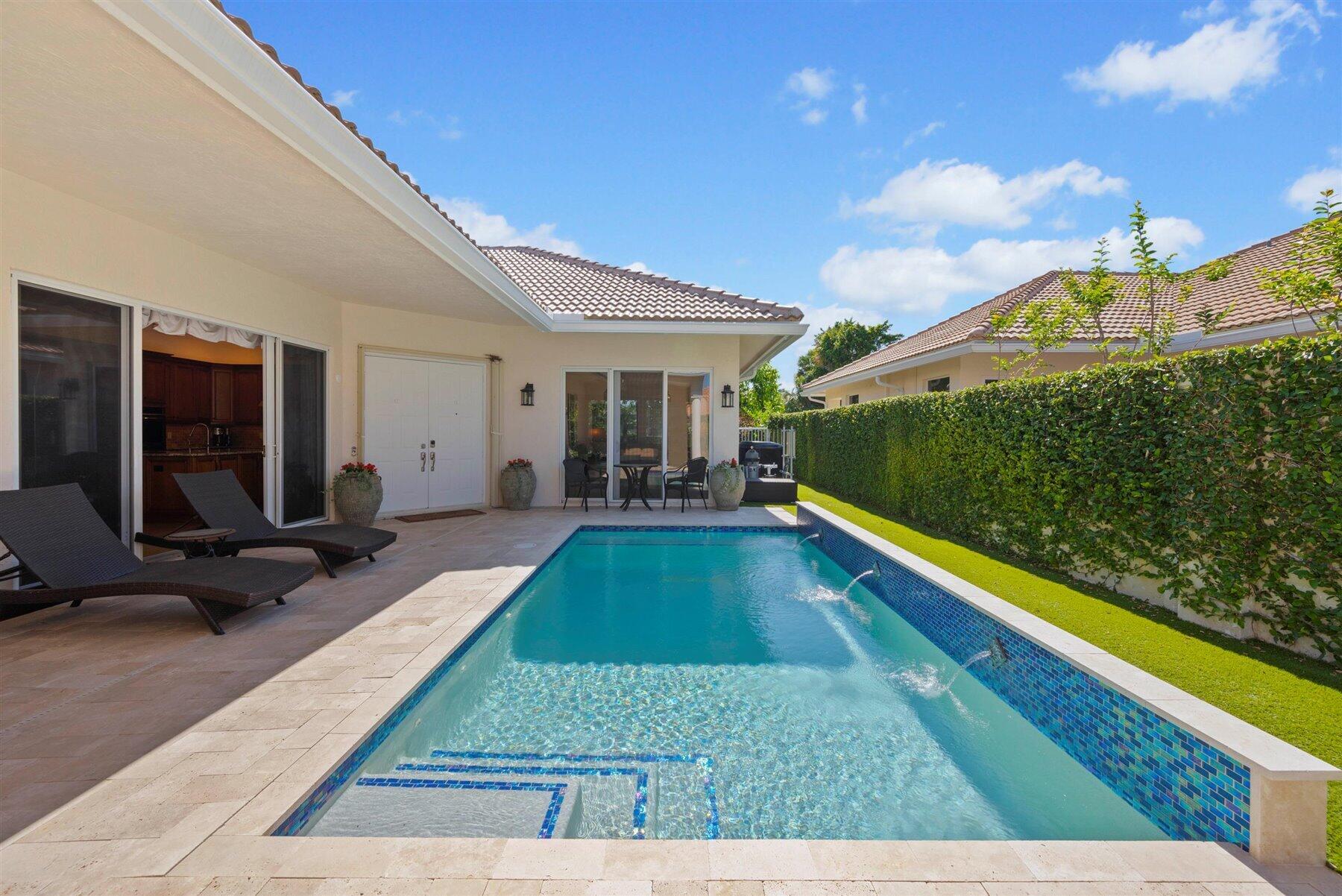 Backyard pool with blue tile, stone patio, lounge chairs, and a hedge-lined lawn.