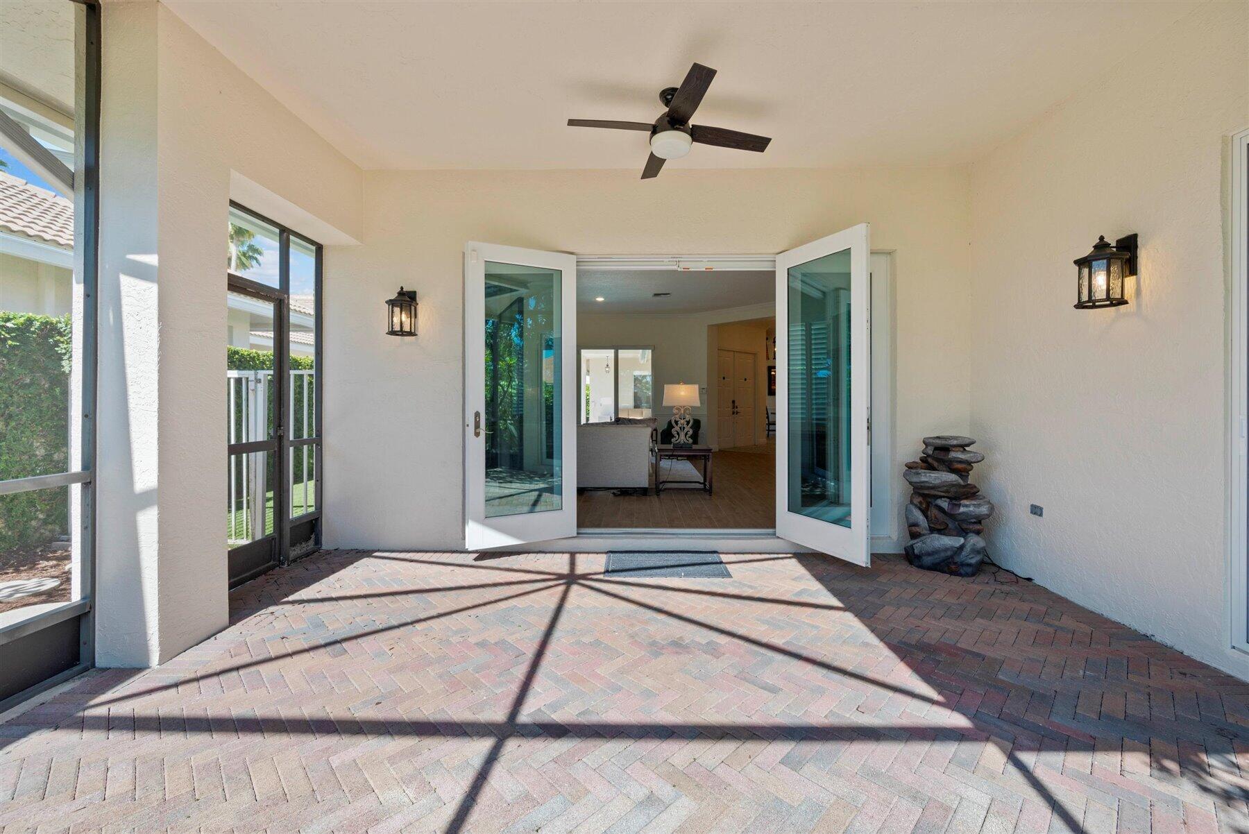 Covered brick patio with open glass doors, a ceiling fan, and a stacked-stone water feature.