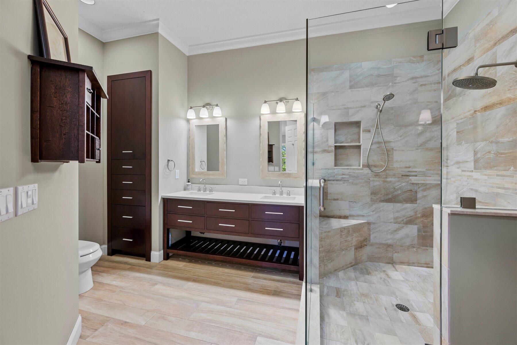 Bathroom with a double vanity and glass-enclosed, stone-tiled walk-in shower.