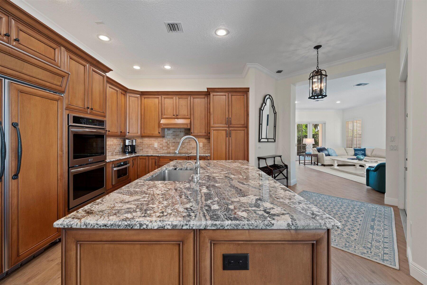 Kitchen with warm wood cabinets and a large granite island, opening onto a bright living room.