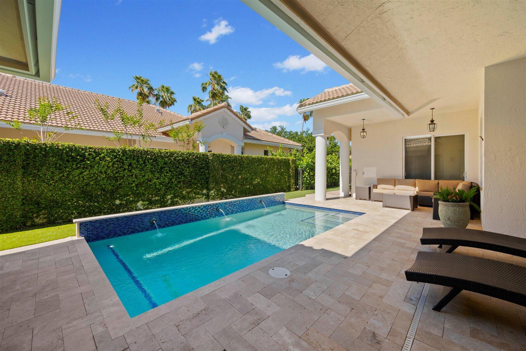 Backyard swimming pool beside a covered patio with lounge seating and a tall privacy hedge.