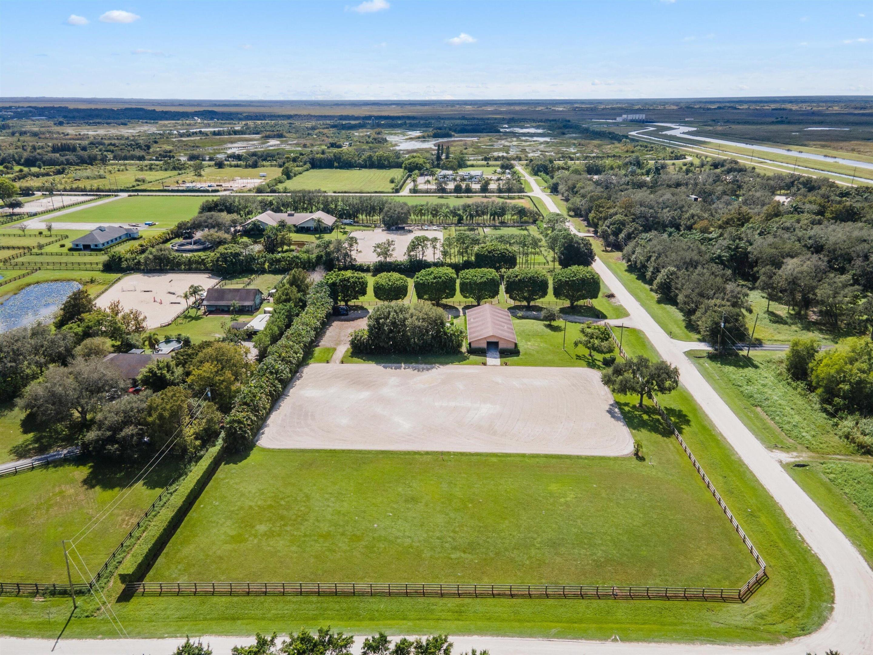 Aerial view of fenced equestrian grounds with a large sand arena and grassy paddocks.