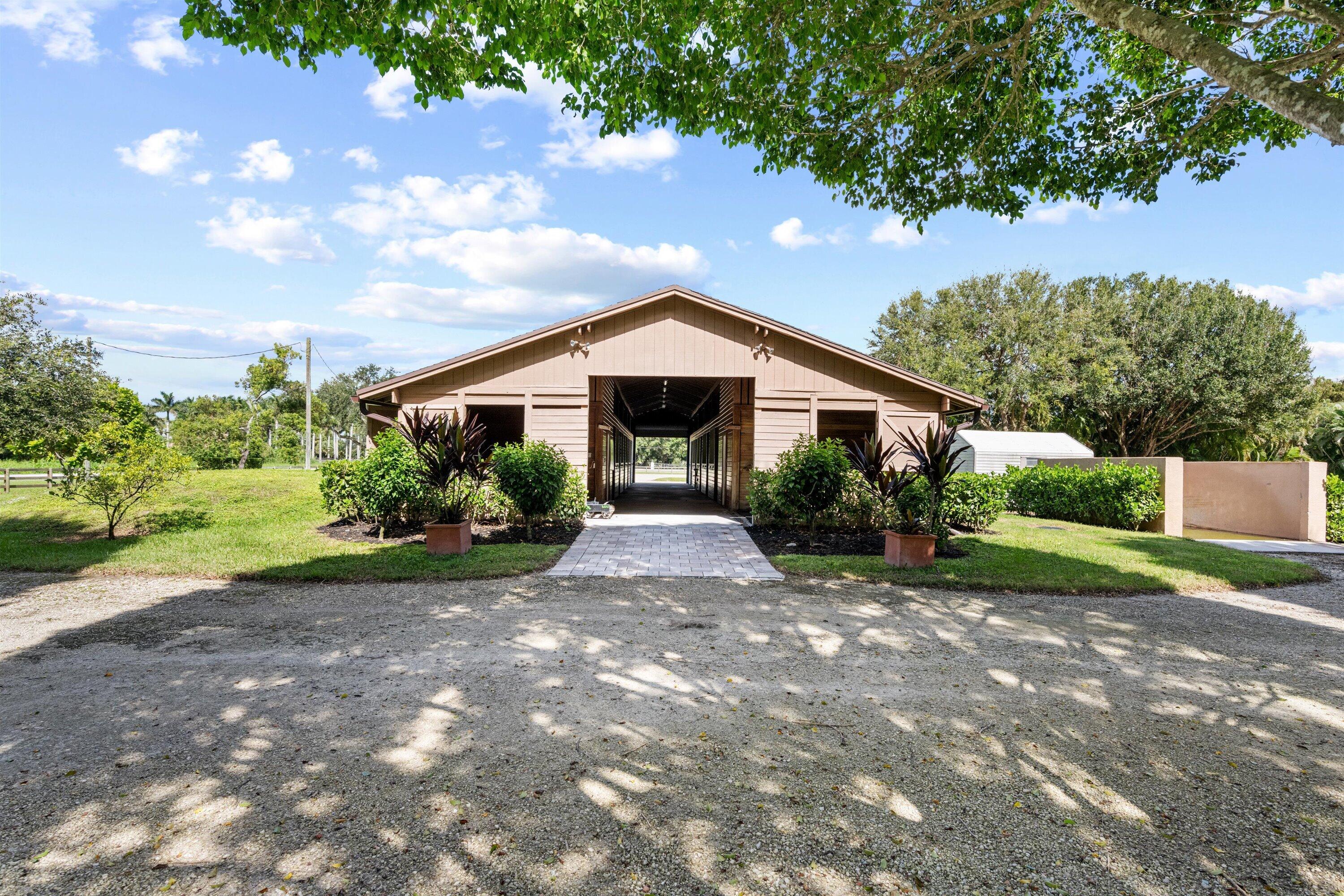 Tan barn with a covered central passage, landscaped entrance, and gravel drive.