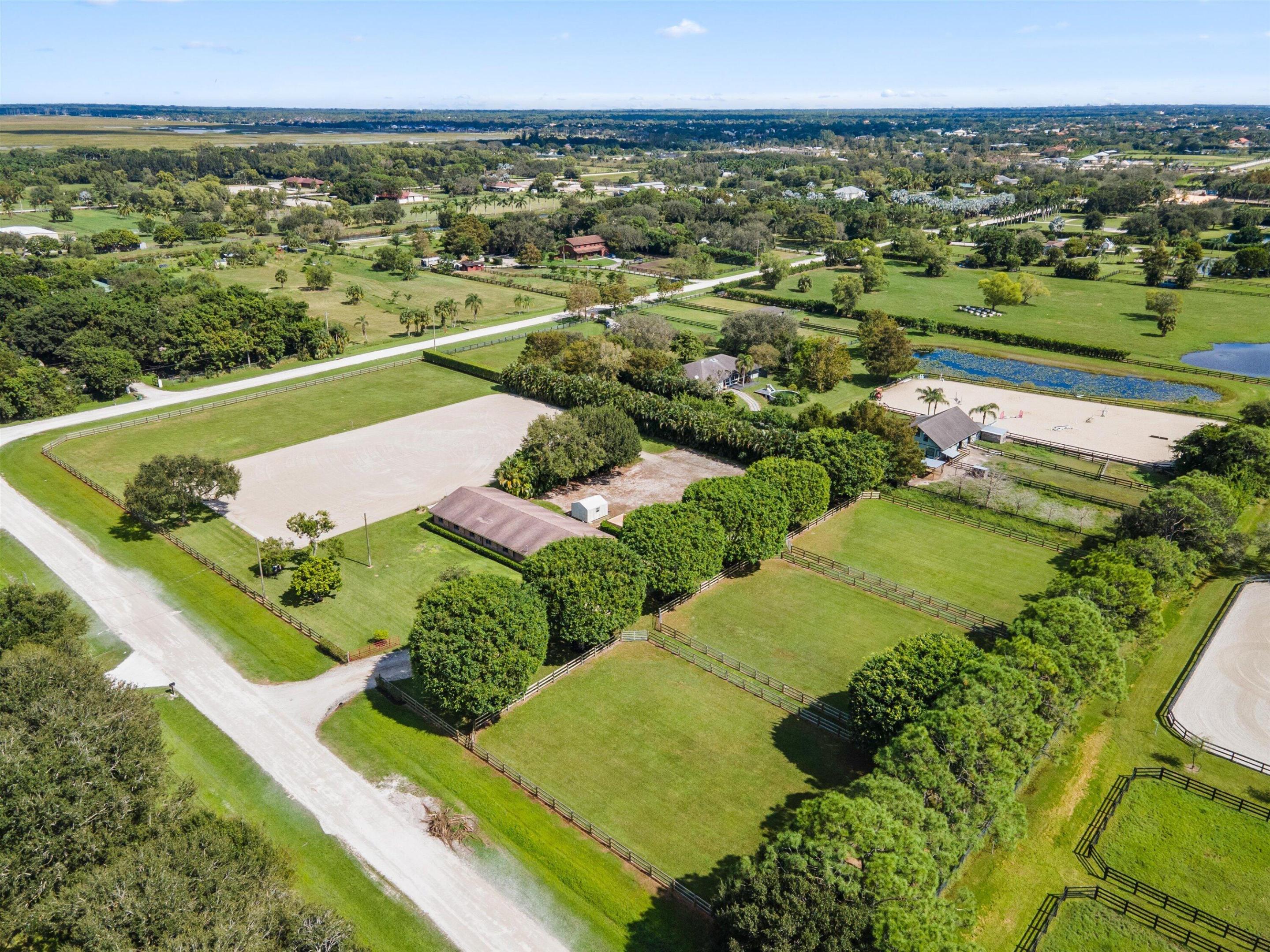 Aerial view of an equestrian property with fenced paddocks, riding arenas, and a tree-lined stable.