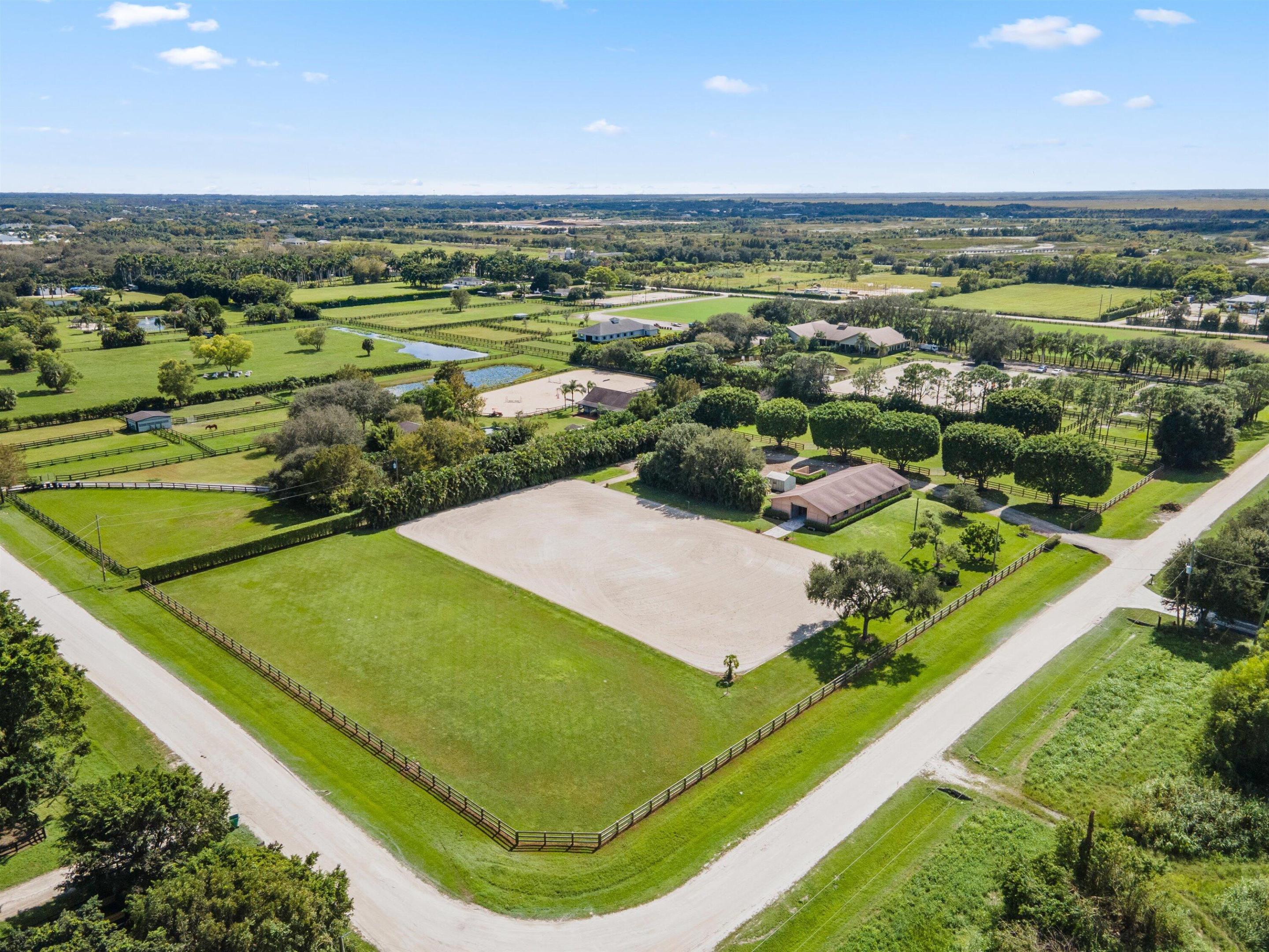 Aerial view of fenced equestrian grounds with paddocks, stable buildings, and a large riding arena.