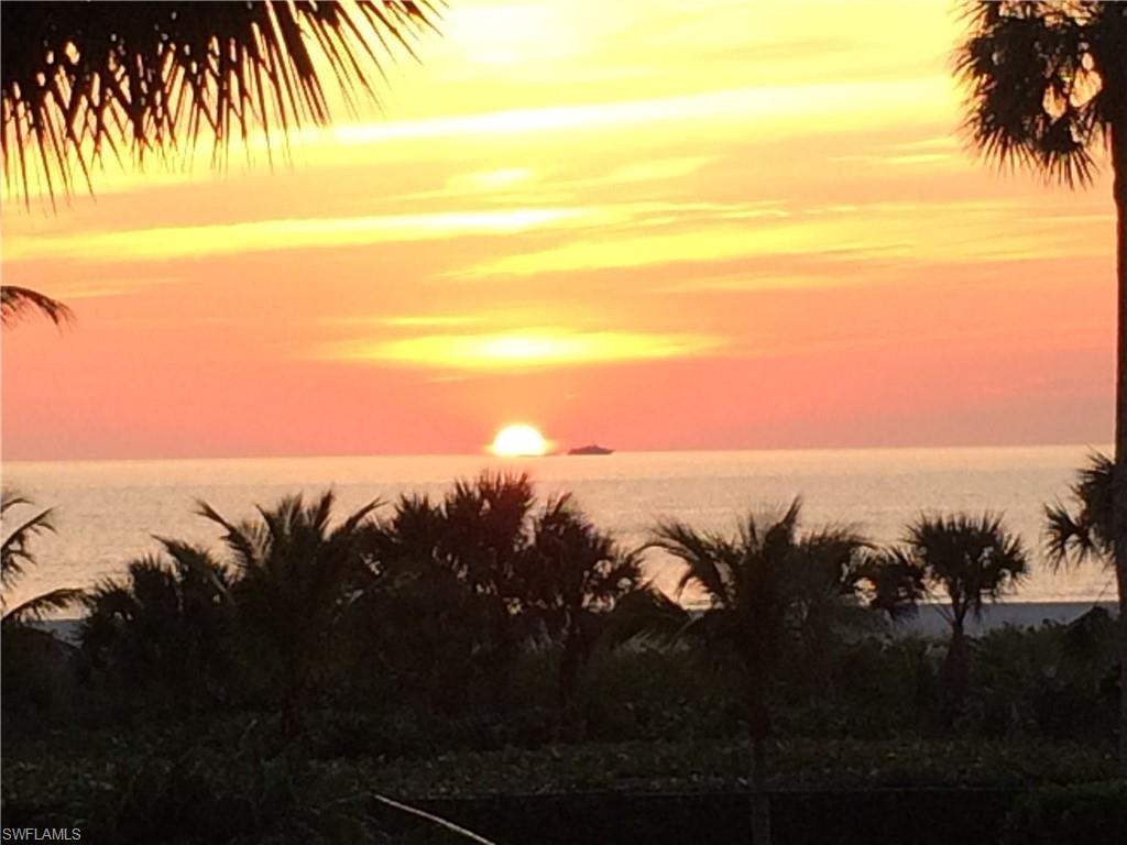 Sunset over the Gulf, framed by palm trees, with a small boat on the horizon.