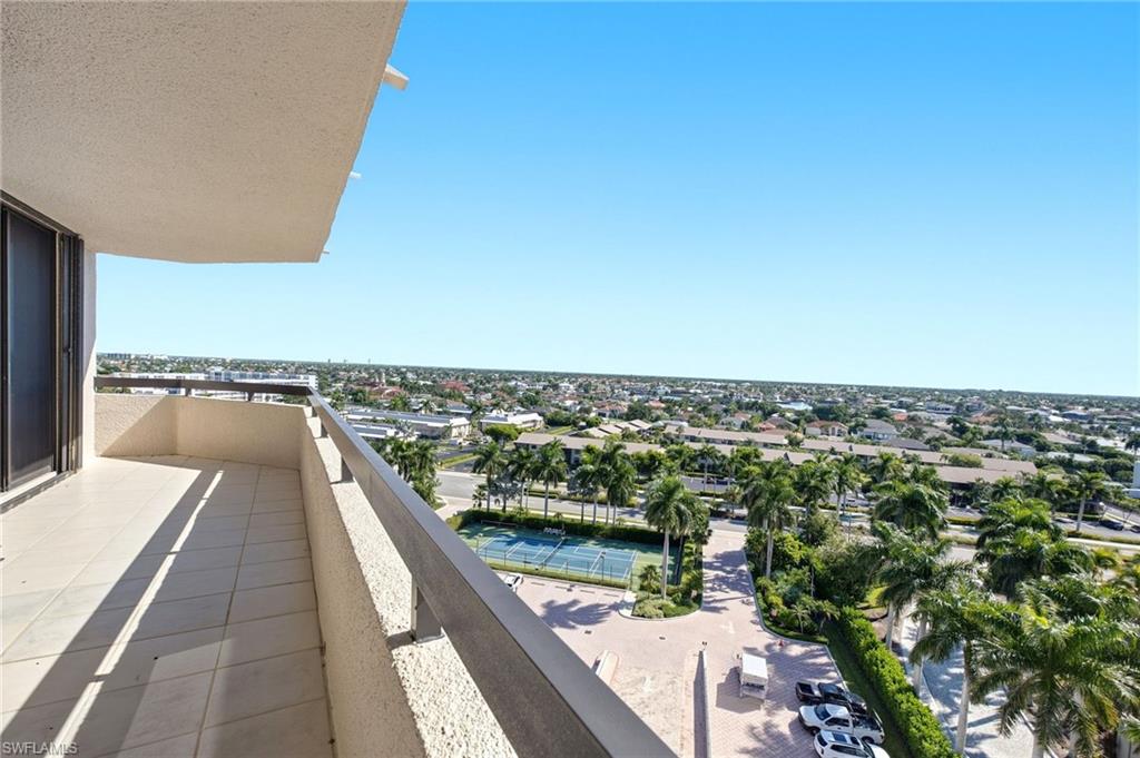 High-rise balcony overlooking palm trees, tennis courts, and low-rise homes.
