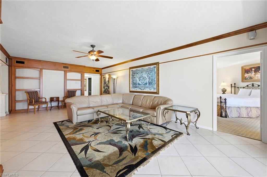 Living room with a cream sectional, patterned rug, built-in wood shelving, and an adjoining bedroom.