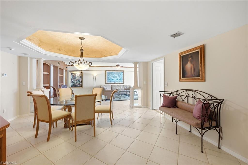 Dining room with a glass-top table and chandelier, opening to a furnished living area.