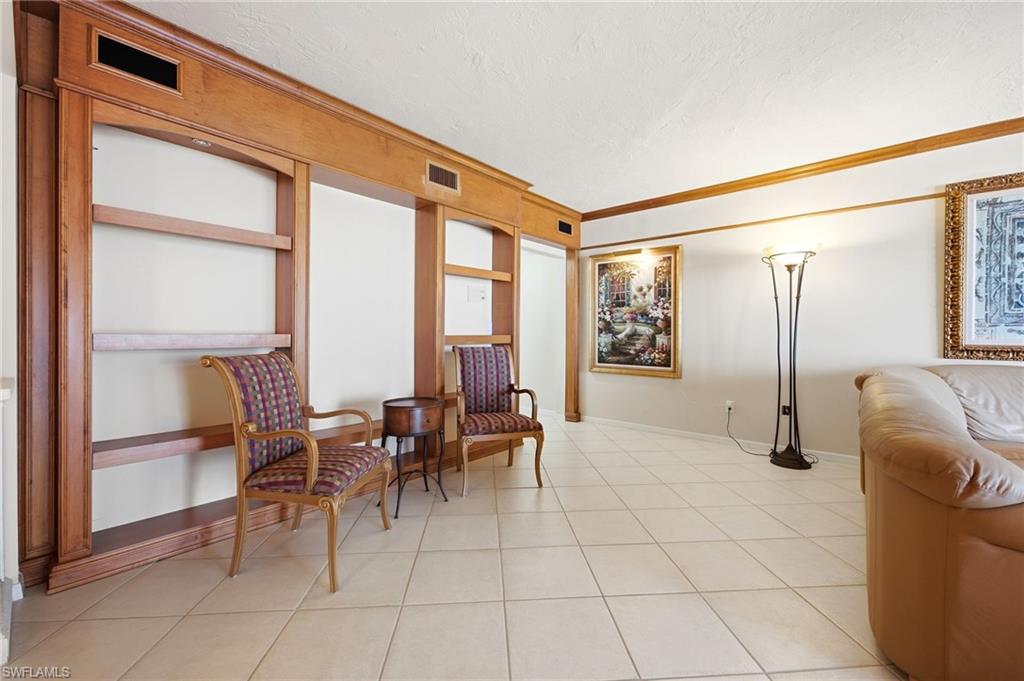 Living room with built-in wood shelving, patterned chairs, white tile floors, and a tan leather sofa.