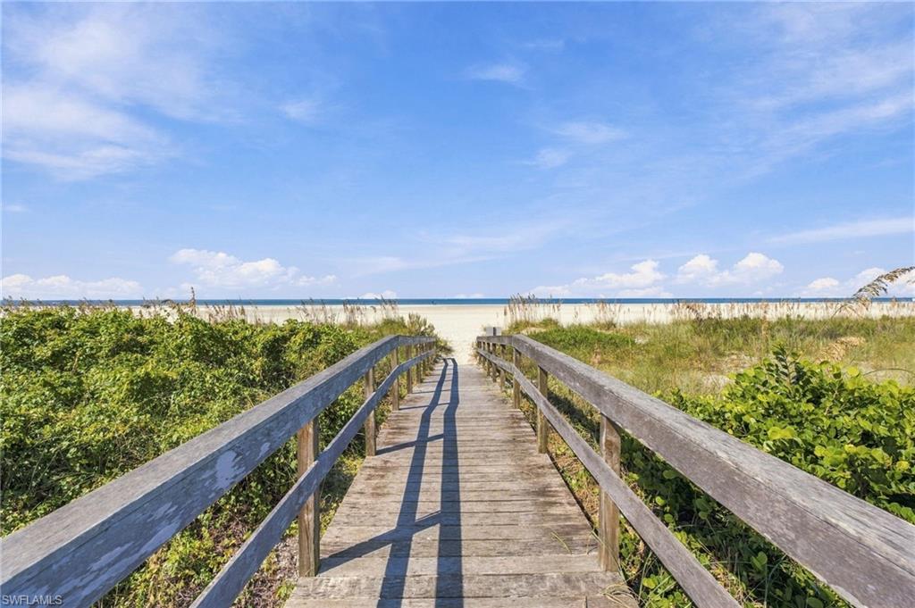 Wooden boardwalk through dune vegetation leads to a sandy beach and ocean.