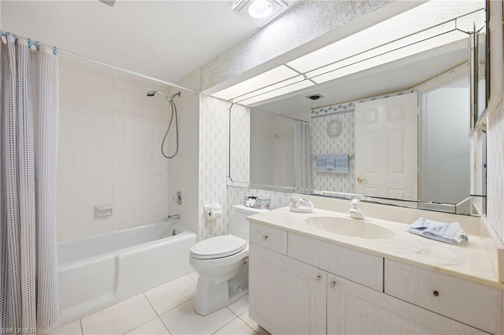 Bathroom with a white bathtub, patterned shower curtain, and long vanity beneath a large mirror.