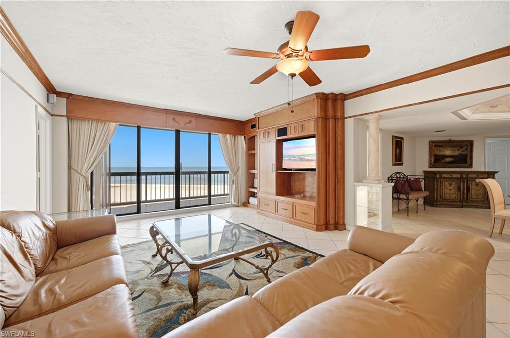 Living room with tan leather sofas, wood built-ins, and sliding doors overlooking the beach and ocean.