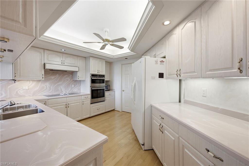 Condominium kitchen with white cabinetry, pale stone counters, built-in double ovens, and light wood flooring.