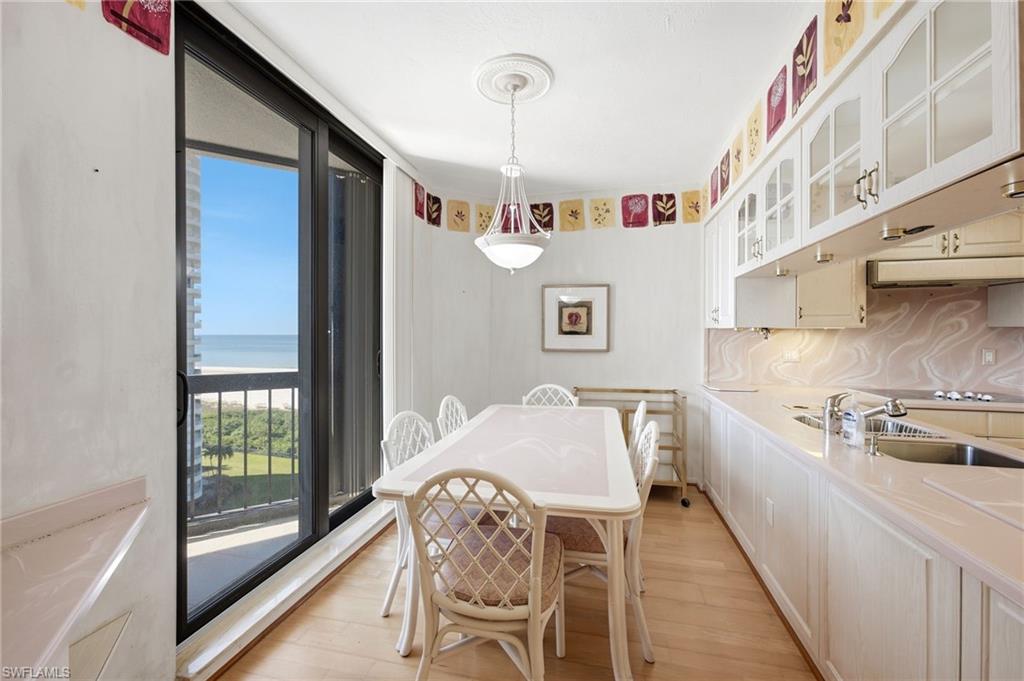 Dining area with white table and chairs, built-in kitchen cabinets, and water visible through sliding glass doors.