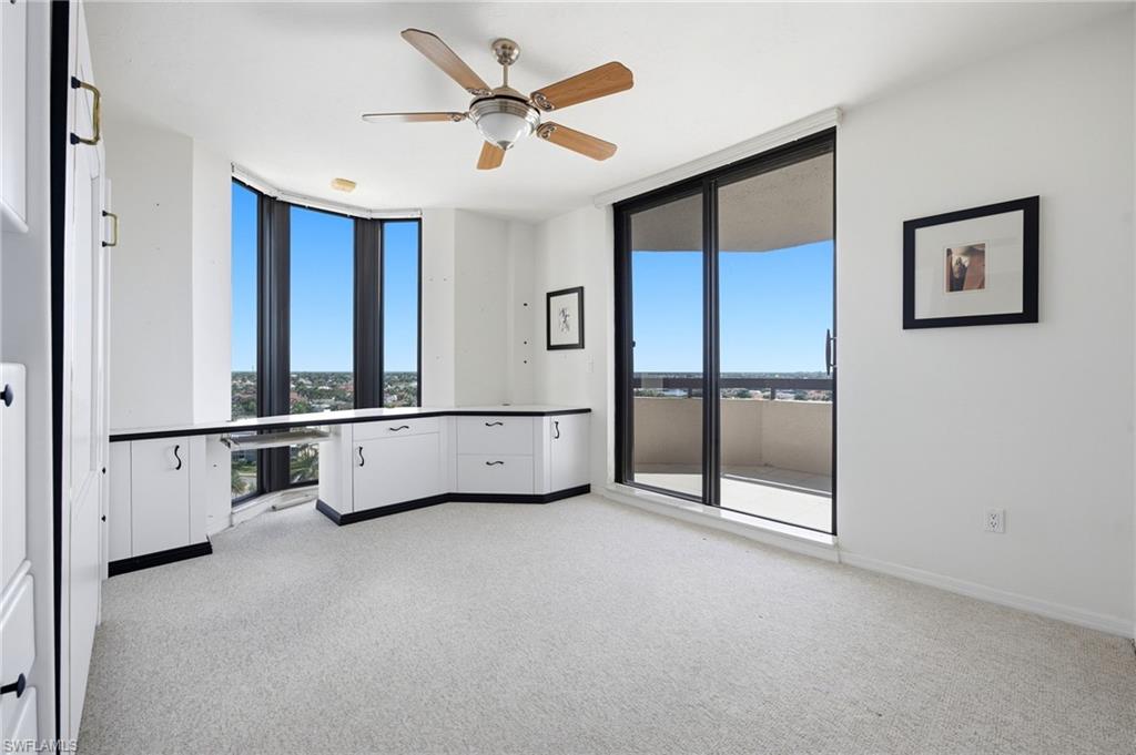 Empty carpeted room with built-in cabinetry, ceiling fan, and sliding doors to a balcony.