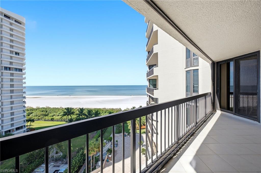 High-rise balcony overlooking Marco Island’s white-sand beach and ocean, with a black railing and tiled floor.
