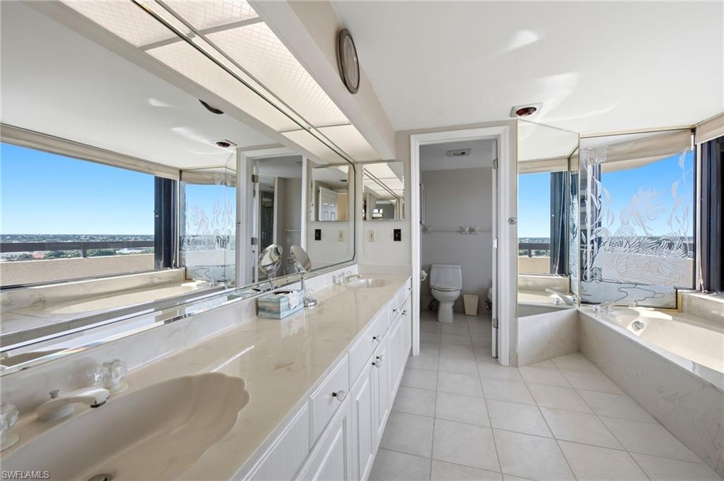 Bright bathroom with a long vanity, built-in soaking tub, and distant water visible through the windows.