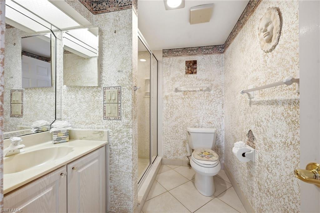 Bathroom with a glass-enclosed shower, white vanity, toilet, and ornate textured walls.