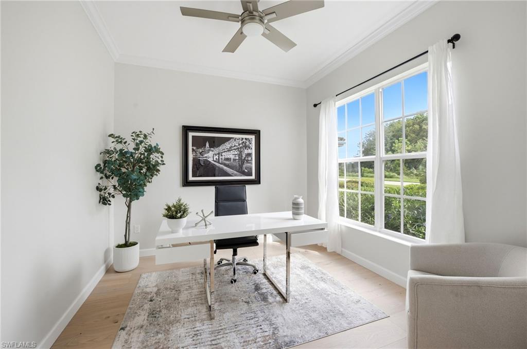 Bright home office with a white desk, large window overlooking greenery, and ceiling fan.