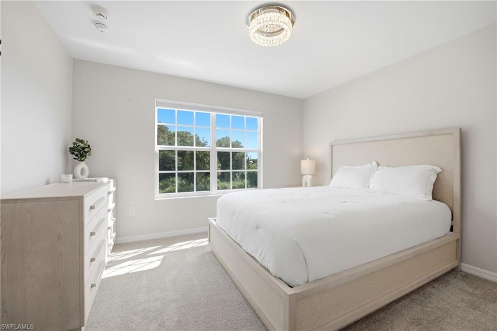 Bright bedroom with a king-size bed, chandelier, and large window overlooking greenery.