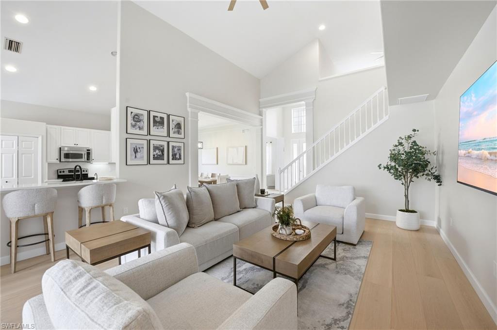 Open-plan living room with gray seating, a white kitchen, and a staircase.