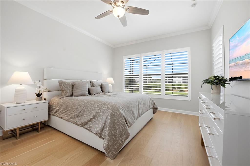 Bedroom with a large gray-covered bed, light wood floors, and plantation-shuttered windows.