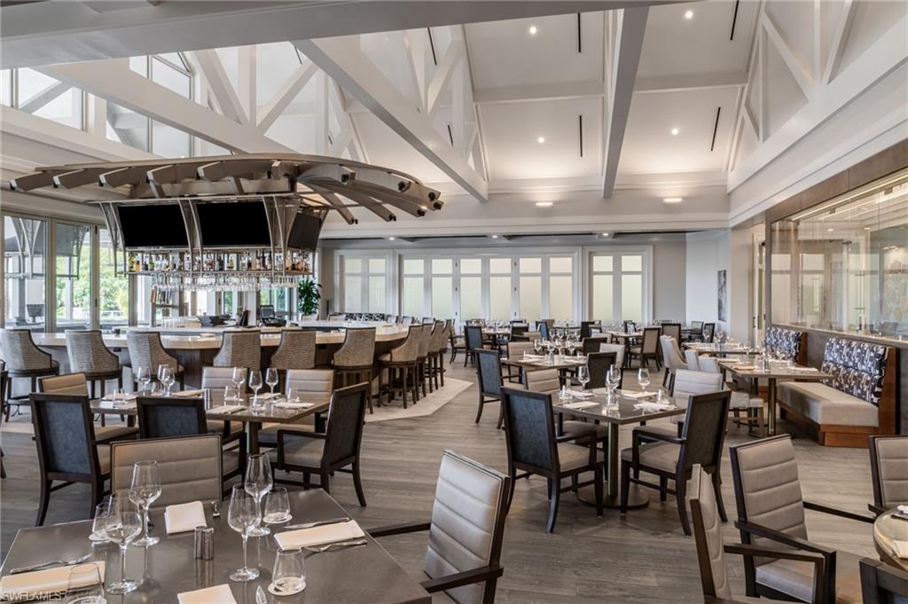 Clubhouse dining room with a curved bar, set tables, and exposed white ceiling trusses.