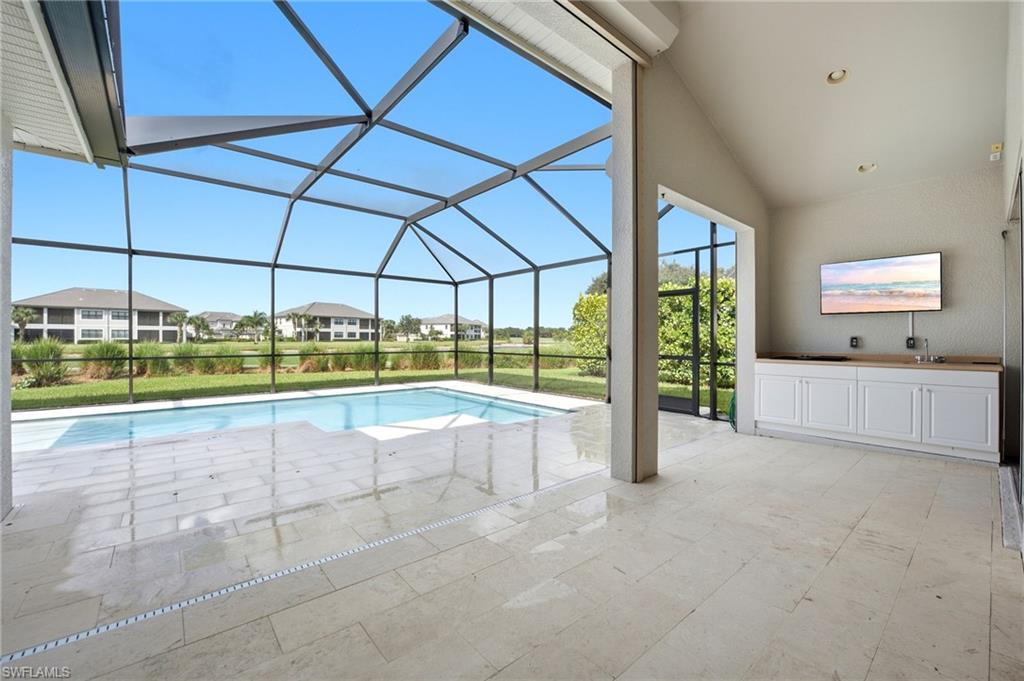 Screened pool lanai with a stone deck and outdoor kitchen counter.