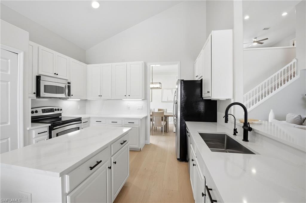 White kitchen with a large island, black fixtures, and light wood floors opening toward the dining area.