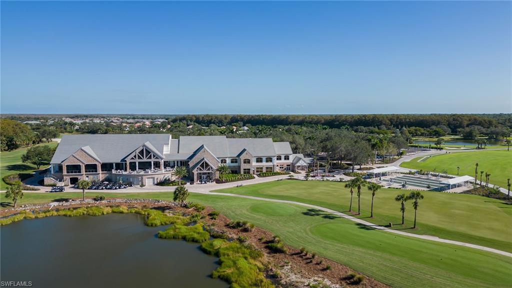 Aerial view of a community clubhouse beside landscaped grounds, courts, and a pond.