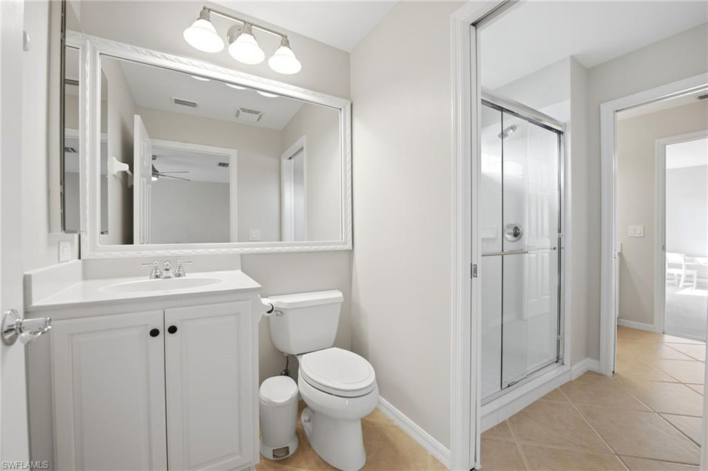 Bathroom with white vanity, large mirror, toilet, and glass-enclosed shower.