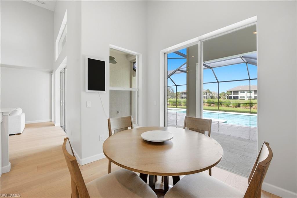 Dining area with a round wood table beside glass doors overlooking a screened pool lanai.