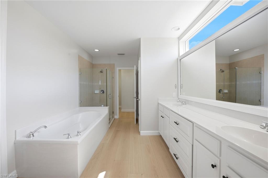 Primary bathroom with a soaking tub, glass shower, and long white double vanity.