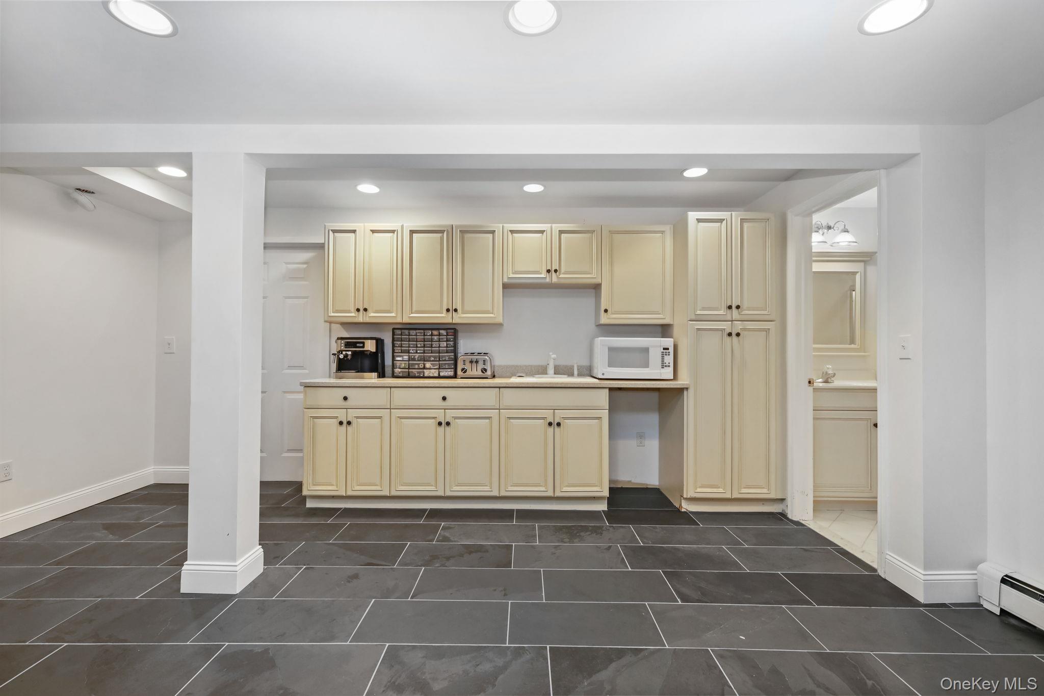 Kitchenette with cream cabinets, dark tile floor, and countertop appliances.
