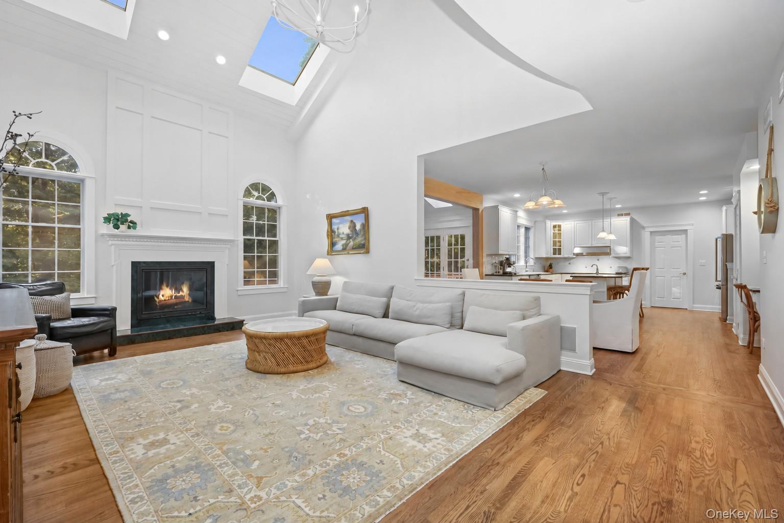Living room with a fireplace, vaulted skylit ceiling, and open kitchen.