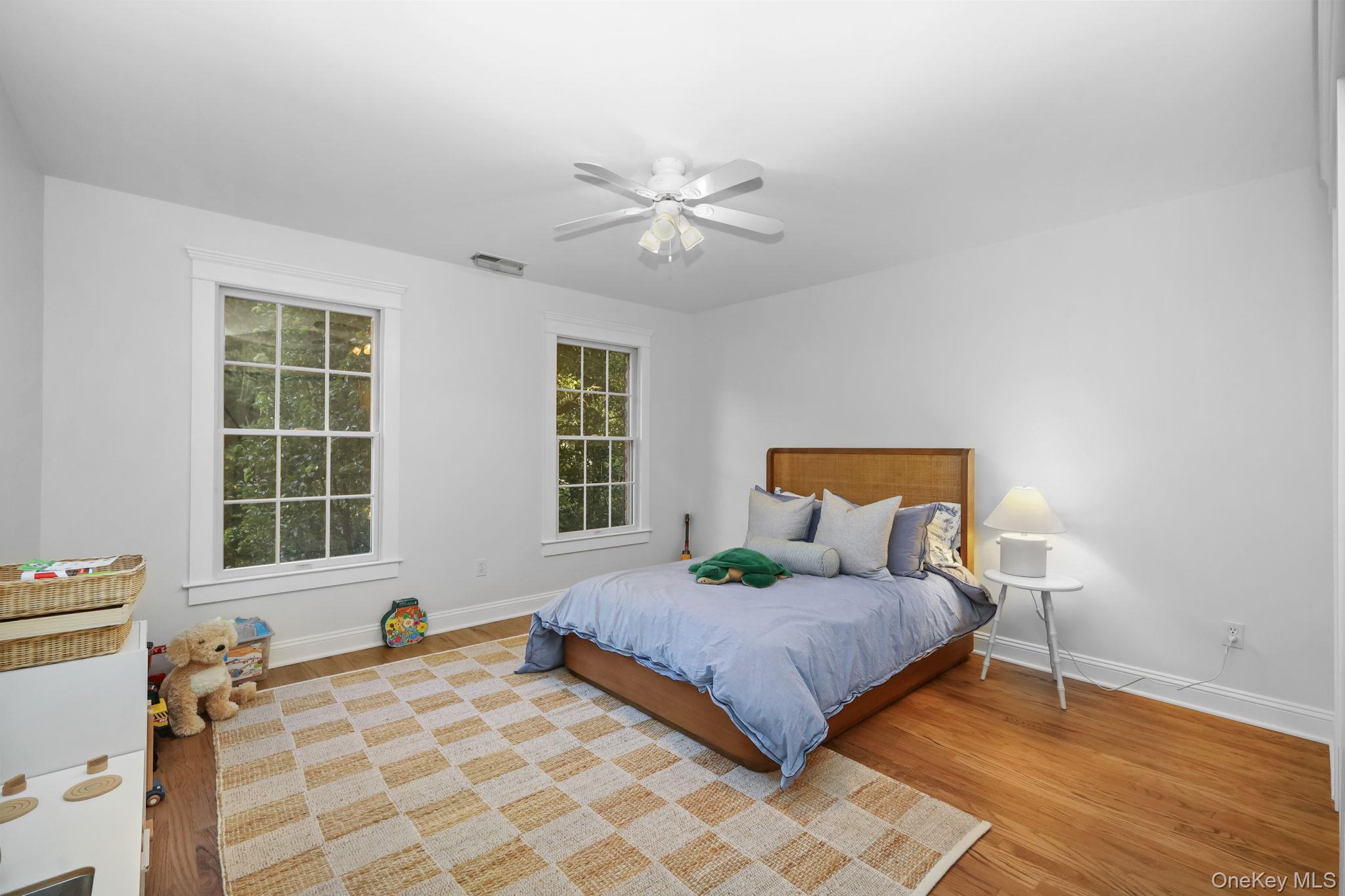 Bedroom with a wooden bed, blue bedding, two tall windows, and a checked rug.