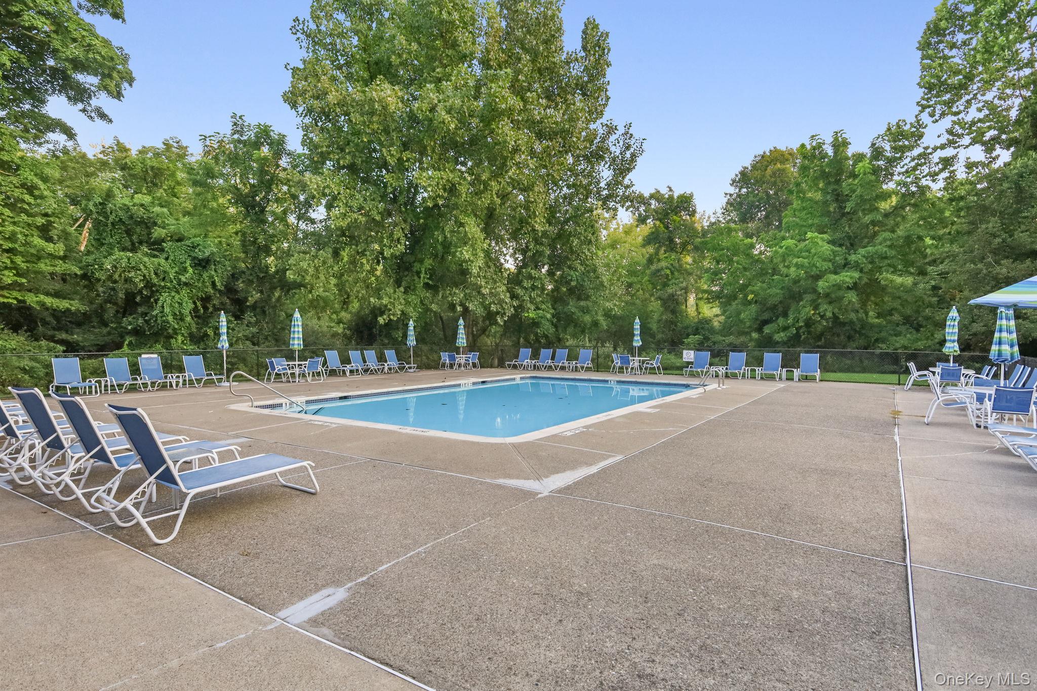 Outdoor swimming pool with blue lounge chairs and umbrellas on a tree-lined deck.