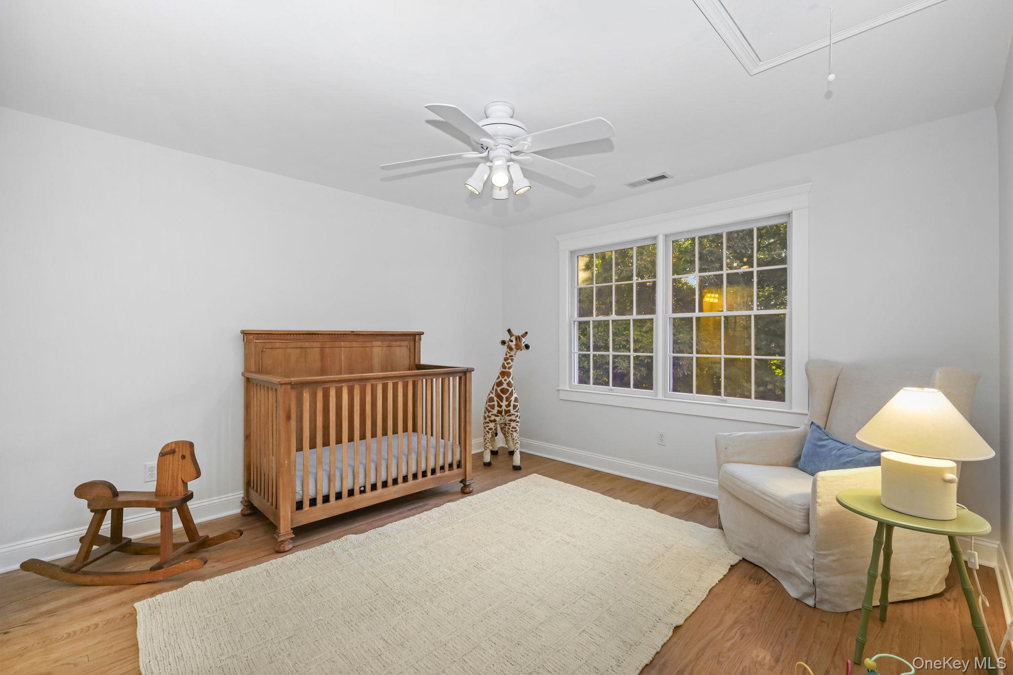 Nursery with a wooden crib, rocking horse, giraffe toy, and large double windows.