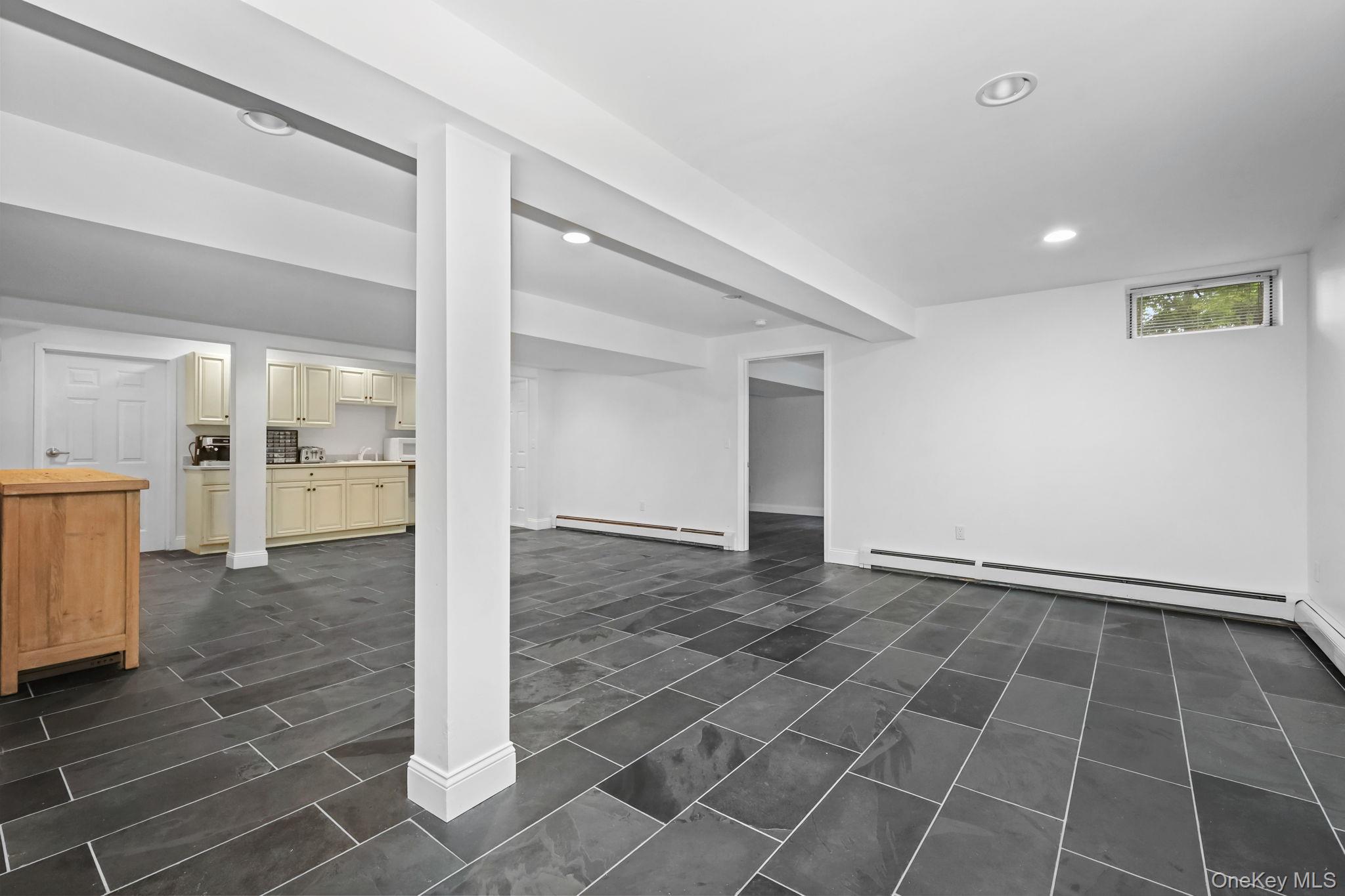 Finished lower-level room with dark tile flooring, a central column, and a small kitchenette.