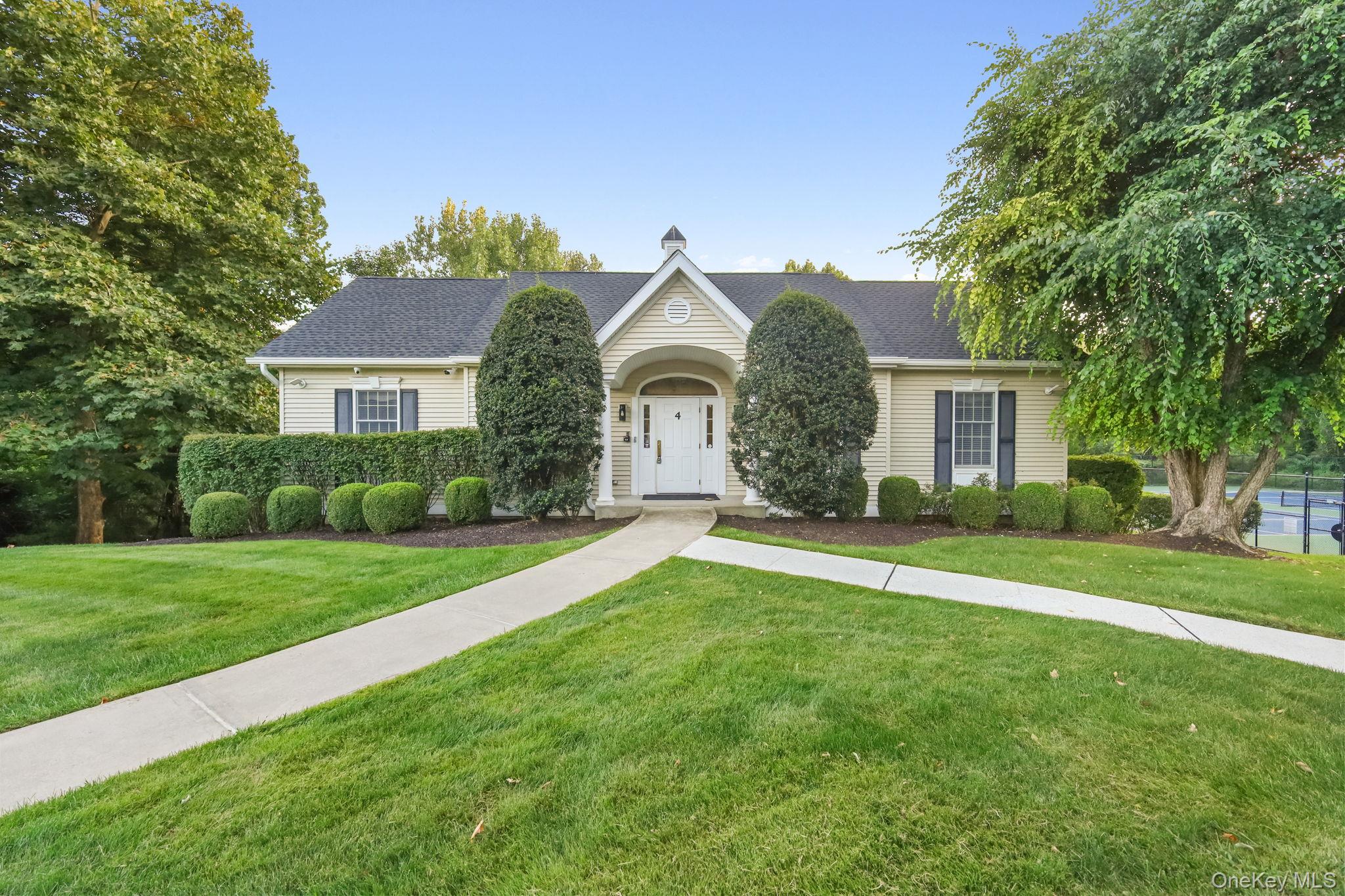 Single-story beige house with an arched entrance, curved walkway, and fenced tennis court.