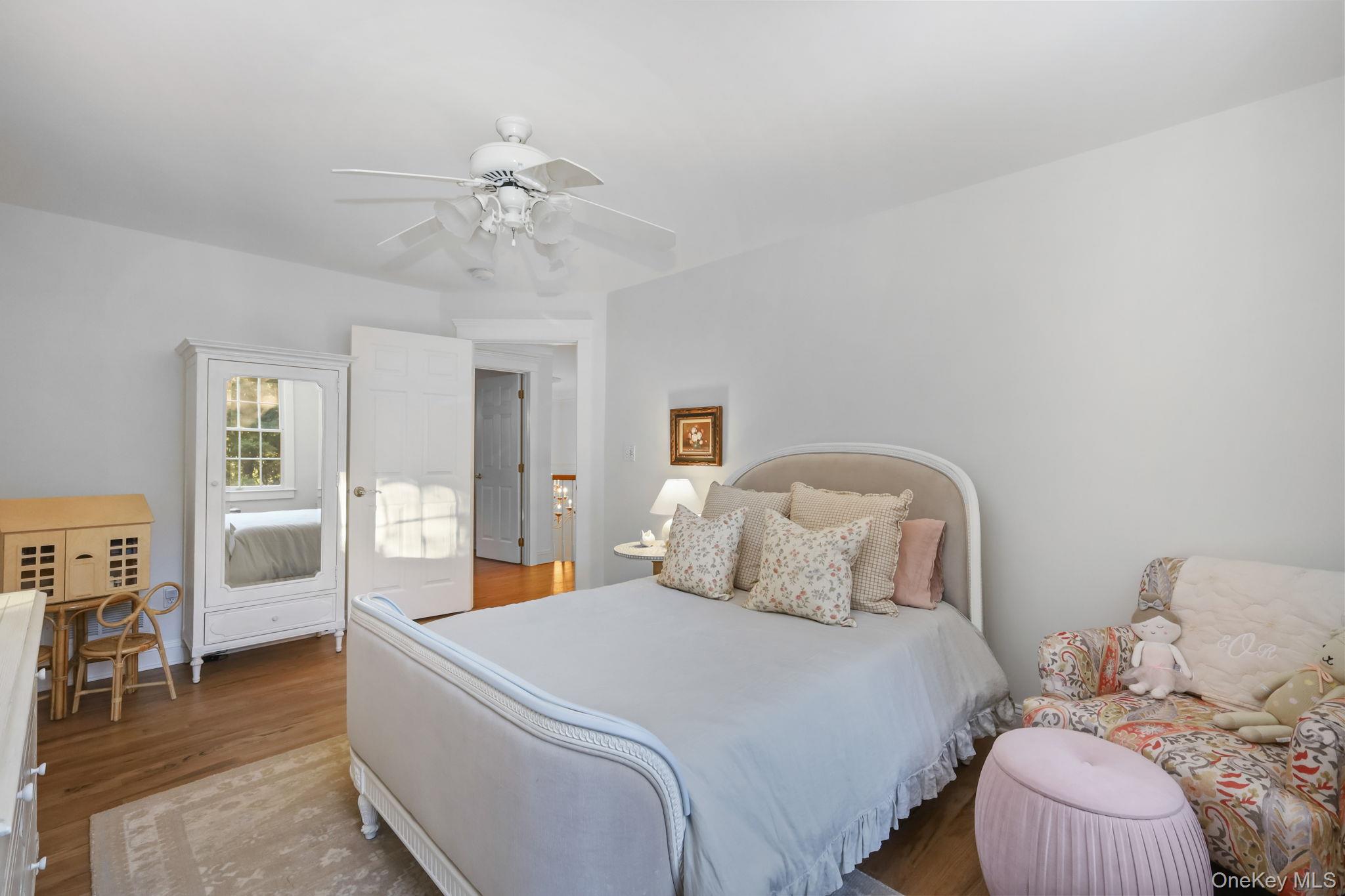 Bedroom with a large bed, mirrored armoire, and floral chair beside a pink ottoman.
