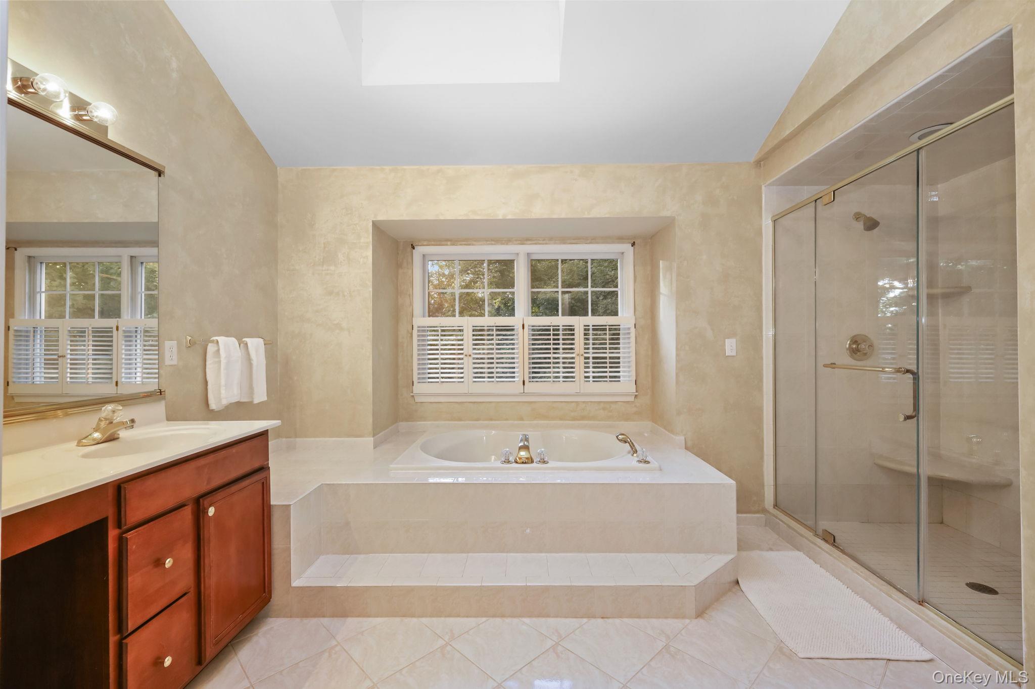 Primary bathroom with a built-in soaking tub beneath shuttered windows and a glass-enclosed shower.