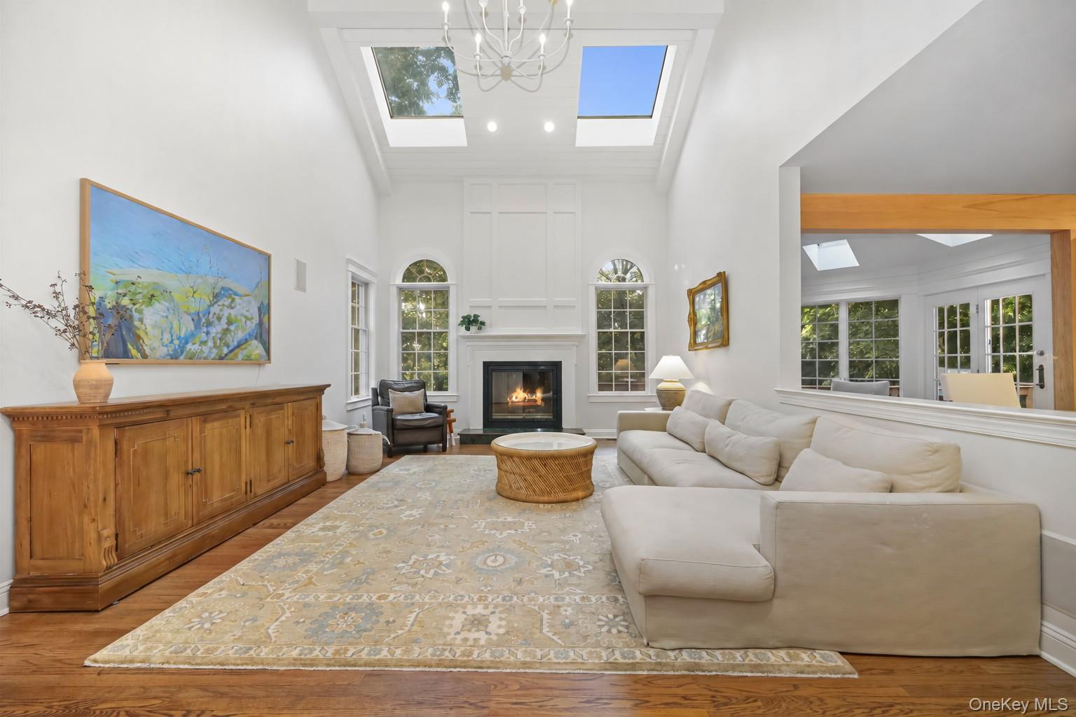 Living room with a vaulted skylit ceiling, lit fireplace, cream sectional, and patterned rug.