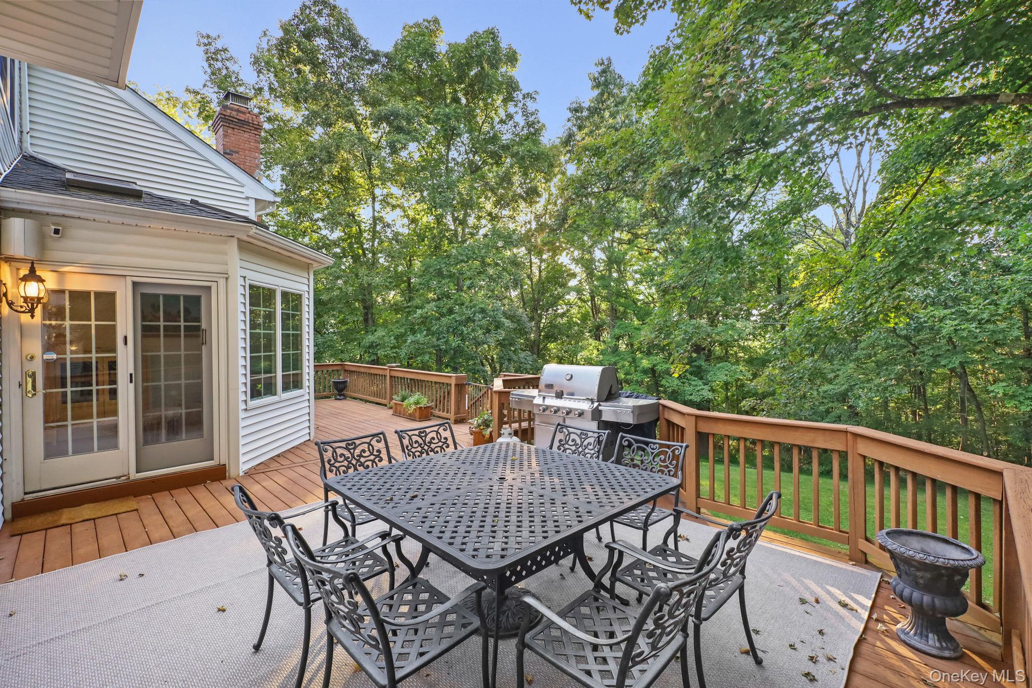 Wooden deck with outdoor dining set and gas grill overlooking a leafy wooded yard.