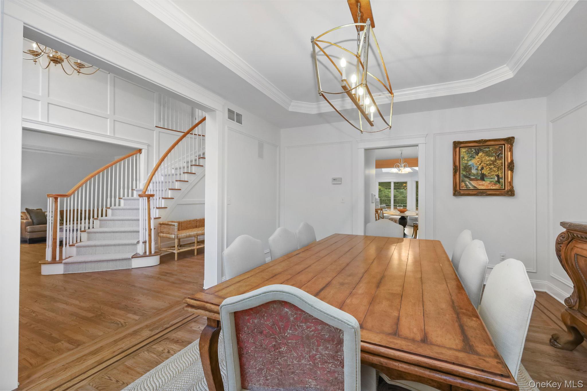 Dining room with a long wooden table beside a carpeted staircase with wood handrails.